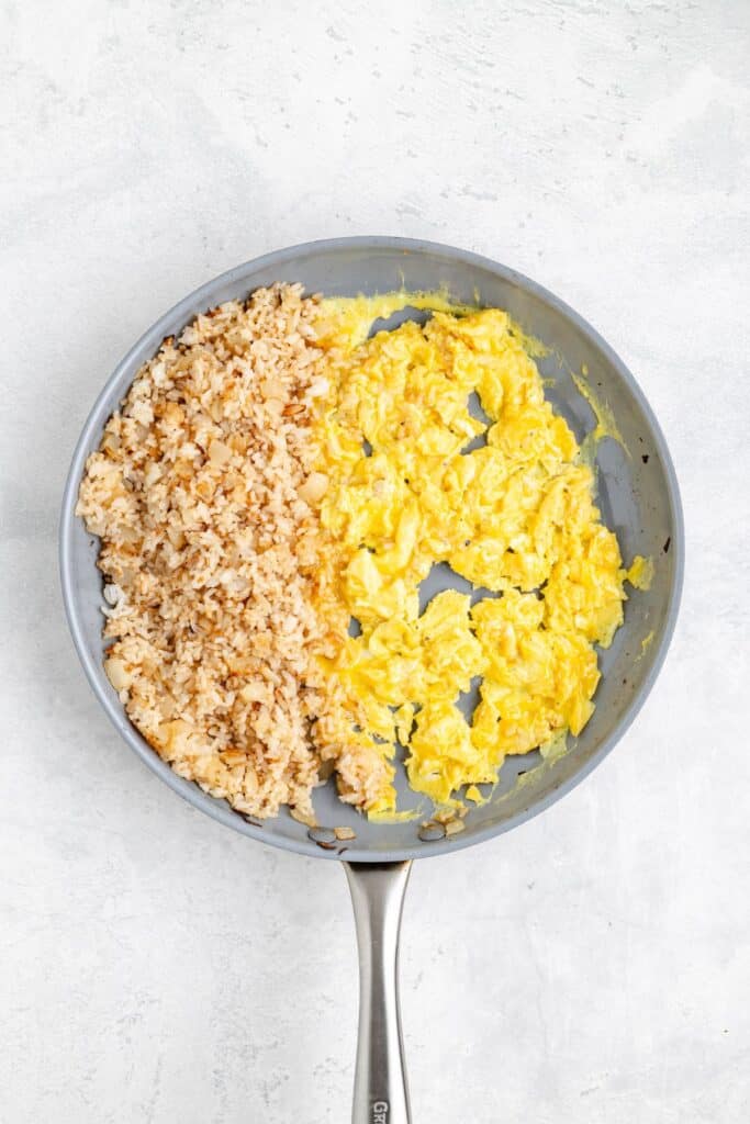 Frying pan with scrambled eggs on one side, cooked rice on the other, on a light surface.
