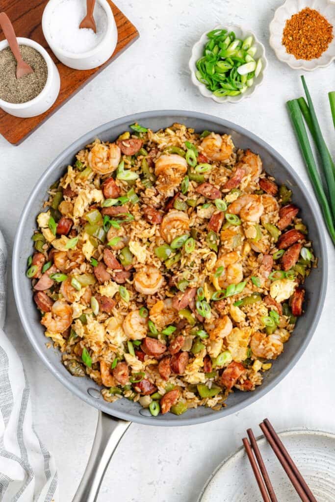 A skillet of Fried Rice with Cajun Seasoning, garnished with green onions; seasonings arranged beside it.