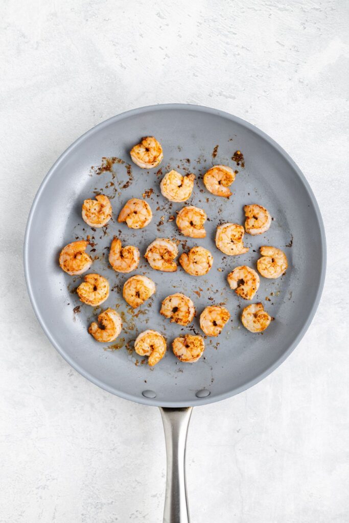 Cooked shrimp in a single layer on a gray nonstick frying pan, browned seasoning visible.