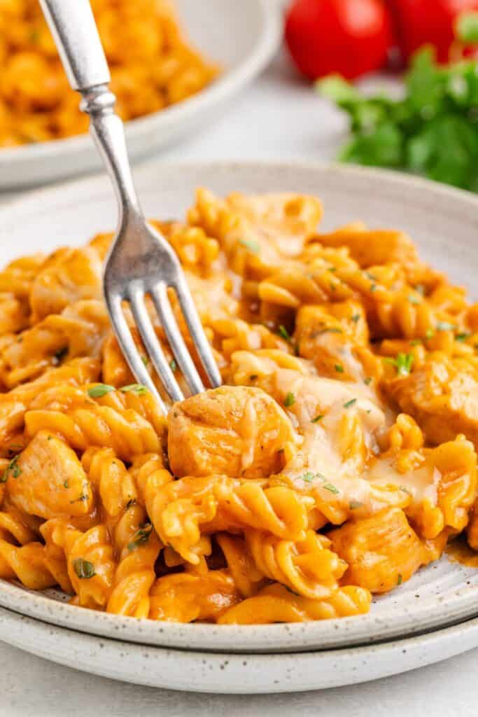 Close-up of creamy rotini pasta with chicken pieces and herbs, fork resting in the dish.