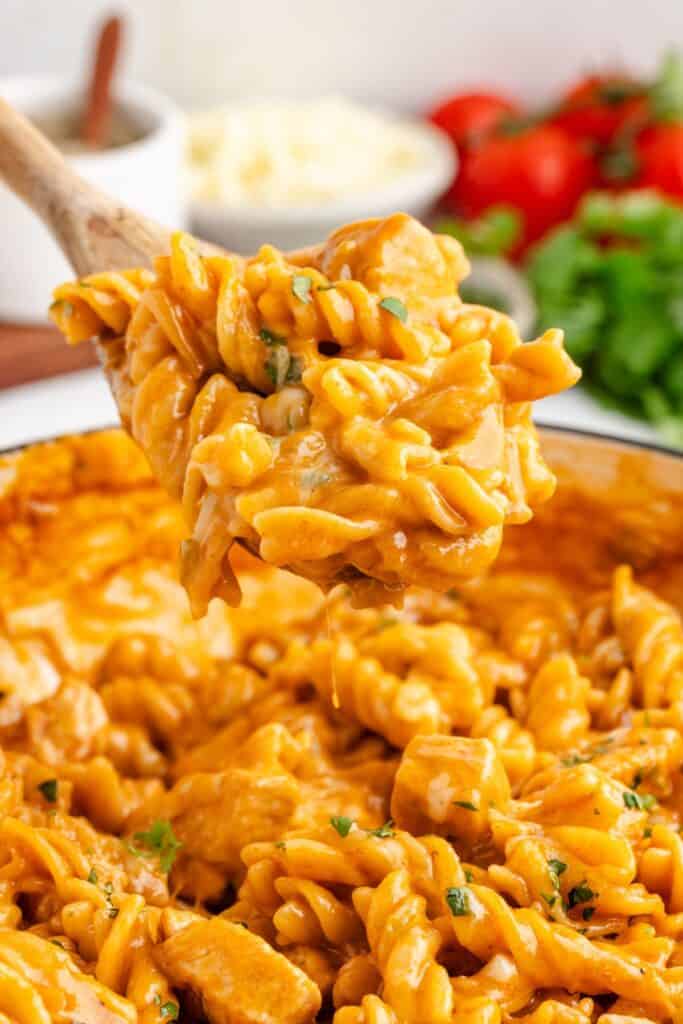 Wooden spoon lifting chicken enchilada pasta from a large pot.