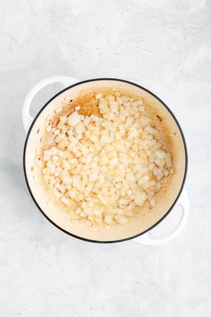 Chopped onions sautéing in a white enameled pot on a light textured countertop.