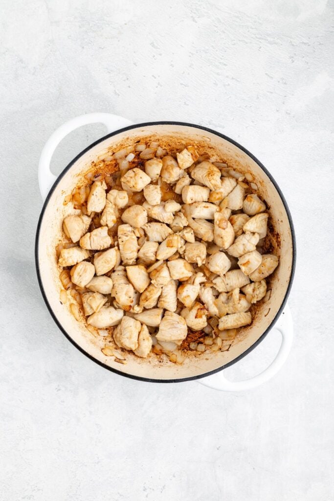 Cubed cooked chicken breast and browned onions in a white pot on a light gray countertop.