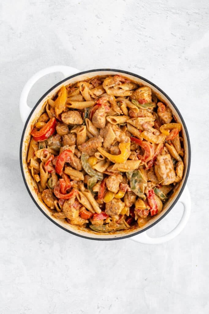 Round white pot of creamy penne pasta with chicken and colorful bell peppers, viewed from above.