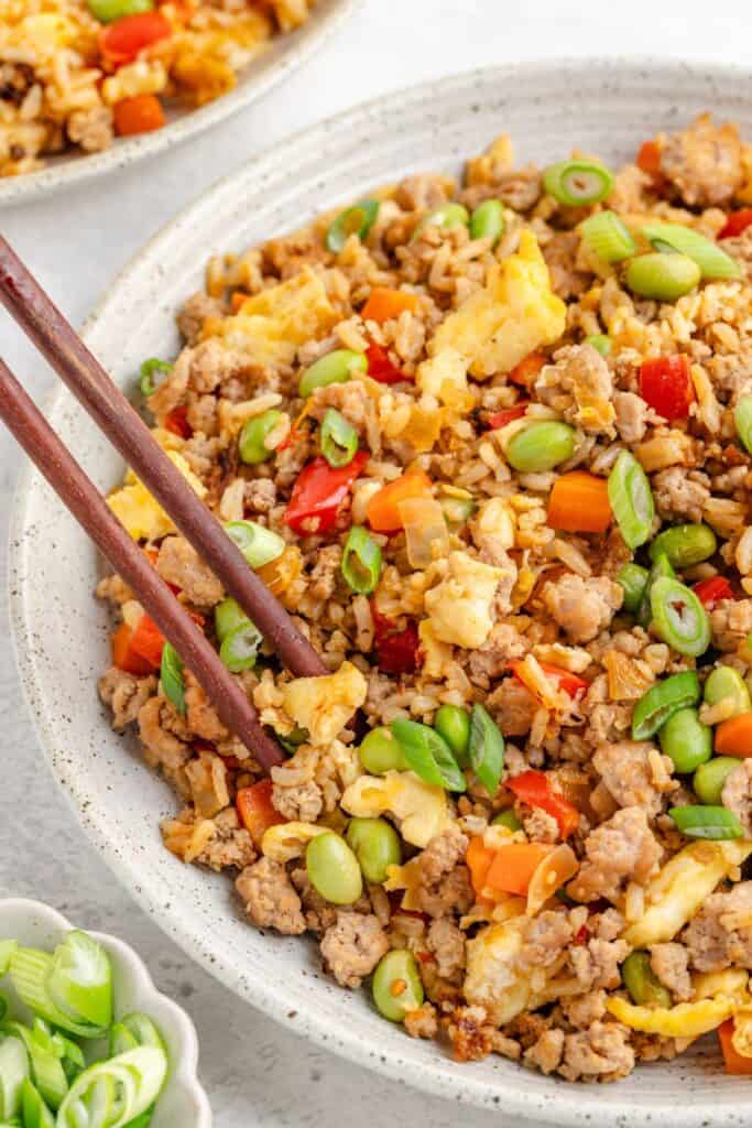 Bowl of fried rice with ground turkey, eggs, vegetables, and chopsticks resting on the side.