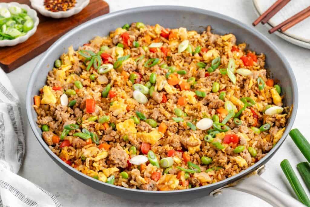 Ground Turkey Fried Rice with ground meat, eggs, carrots, peas, and green onions in a skillet; chopsticks and condiments nearby.