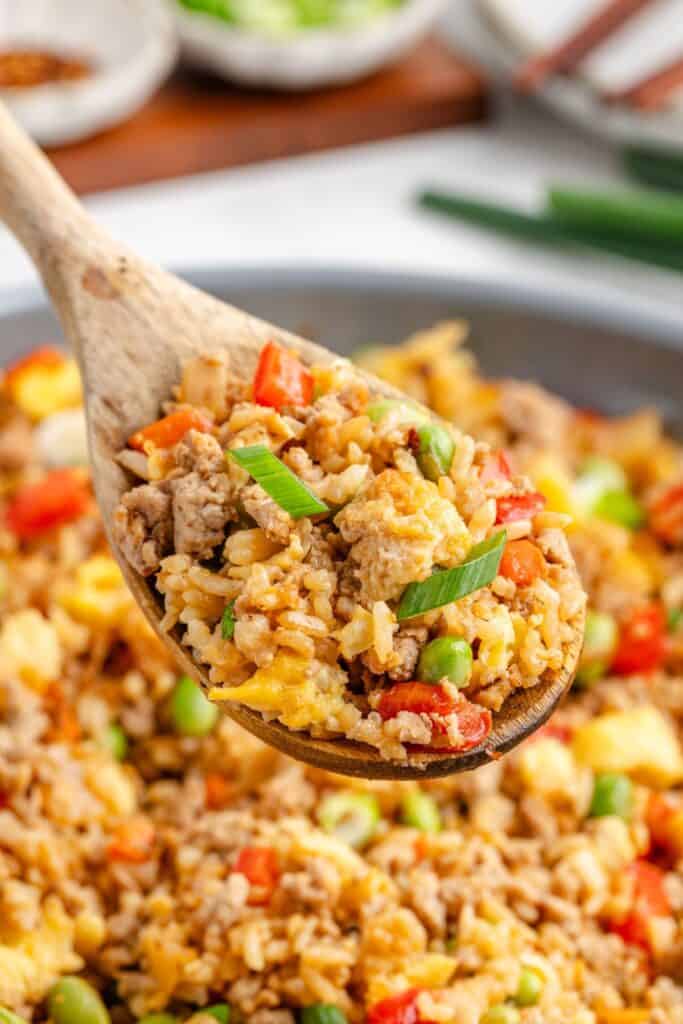 Wooden spoon holding ground turkey fried rice with, scrambled eggs, edamame, red bell peppers, and green onions.