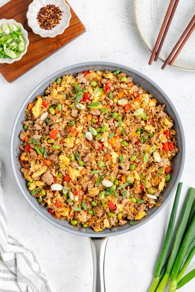 A skillet of ground turkey fried rice with eggs, green onions; chopsticks, plates, and condiments beside it.