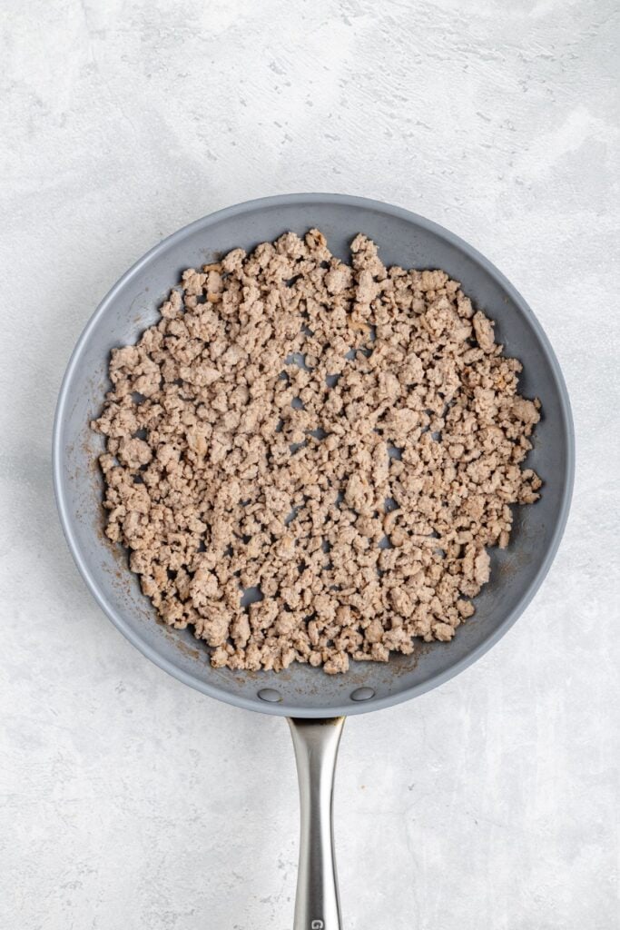 Cooked ground turkey in a nonstick frying pan sits on a light gray countertop.