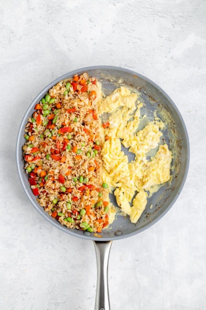 A skillet with fried rice and vegetables on one side, scrambled eggs on the other, on a light surface.