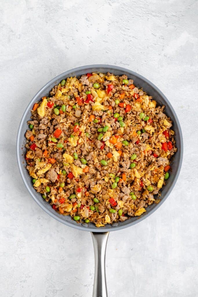 Skillet with ground meat, scrambled eggs, peas, carrots, and red bell peppers mixed on a light background.