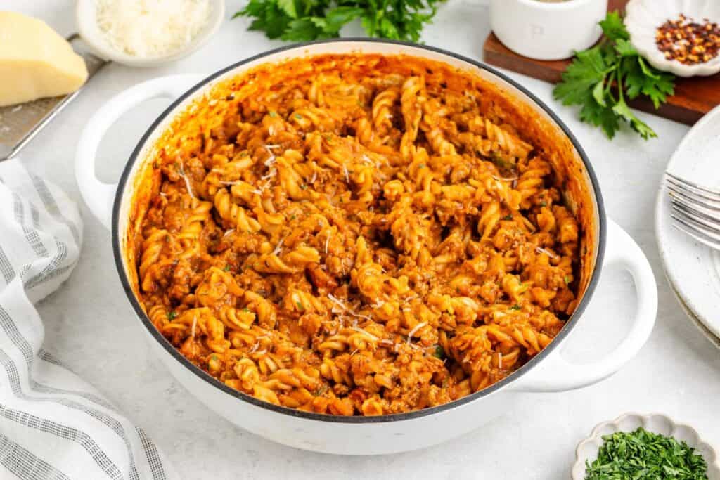 White pot of rotini pasta with ground turkey, tomato sauce, and grated cheese on top.
