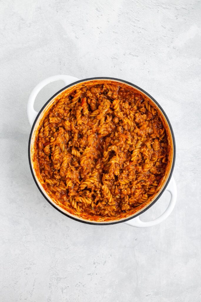 White pot filled with fusilli pasta, ground turkey, and tomato sauce on a light gray surface.