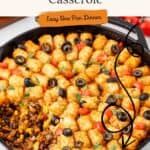 Skillet of Mexican tater tot casserole topped with black olives, tomatoes, herbs; ground meat and corn underneath.