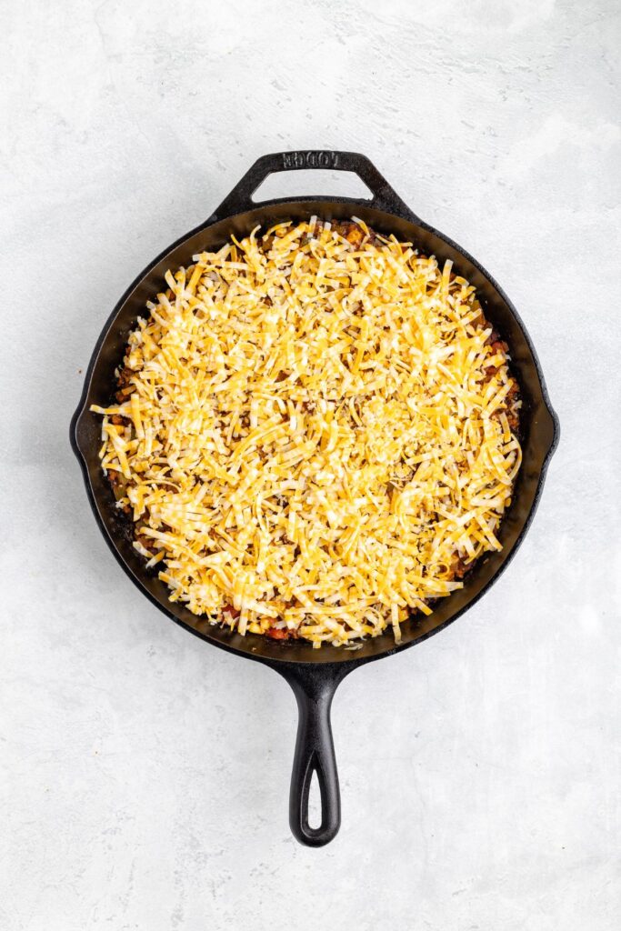Cast iron skillet with shredded cheese atop a casserole, seen from an overhead view.