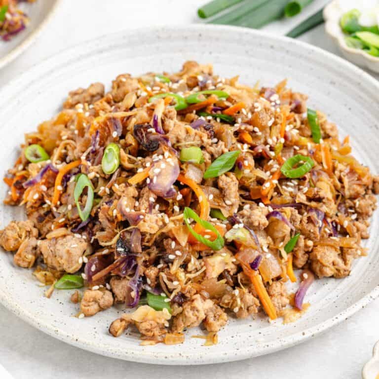 Egg Roll in a Bowl with Ground Pork, cabbage, carrots, onions, and sesame seeds on a white plate.