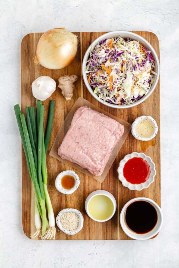 Ground Pork Egg Roll in a Bowl ingredients: ground meat, coleslaw mix, green onions, onion, garlic, ginger, sauces on wooden board.