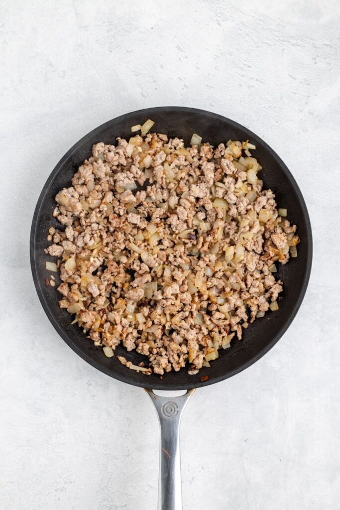 Frying pan with cooked ground meat and diced onions on a light surface.