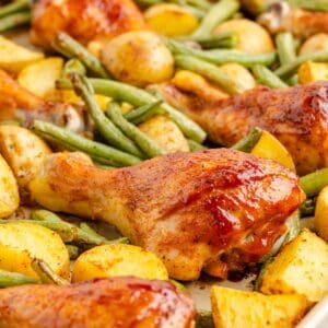 Sheet Pan BBQ chicken drumsticks with golden potatoes and green beans arranged on a baking sheet.