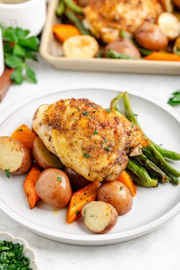 Roasted chicken thighs with green beans, red potatoes, and carrots on a plate, garnished with fresh herbs.