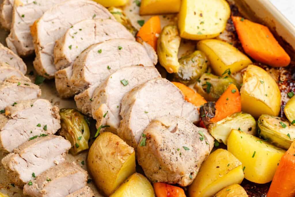 Sliced sheet pan pork tenderloin with roasted potatoes, carrots, and Brussels sprouts.