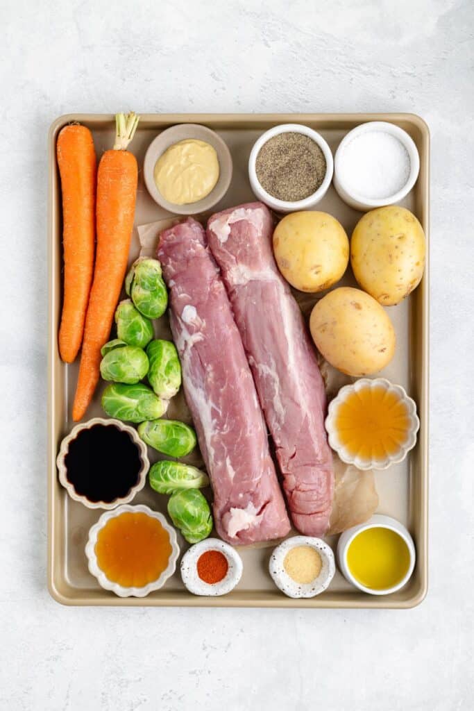 Raw pork tenderloin, carrots, potatoes, Brussels sprouts on a tray with bowls of oil, seasonings, and honey.