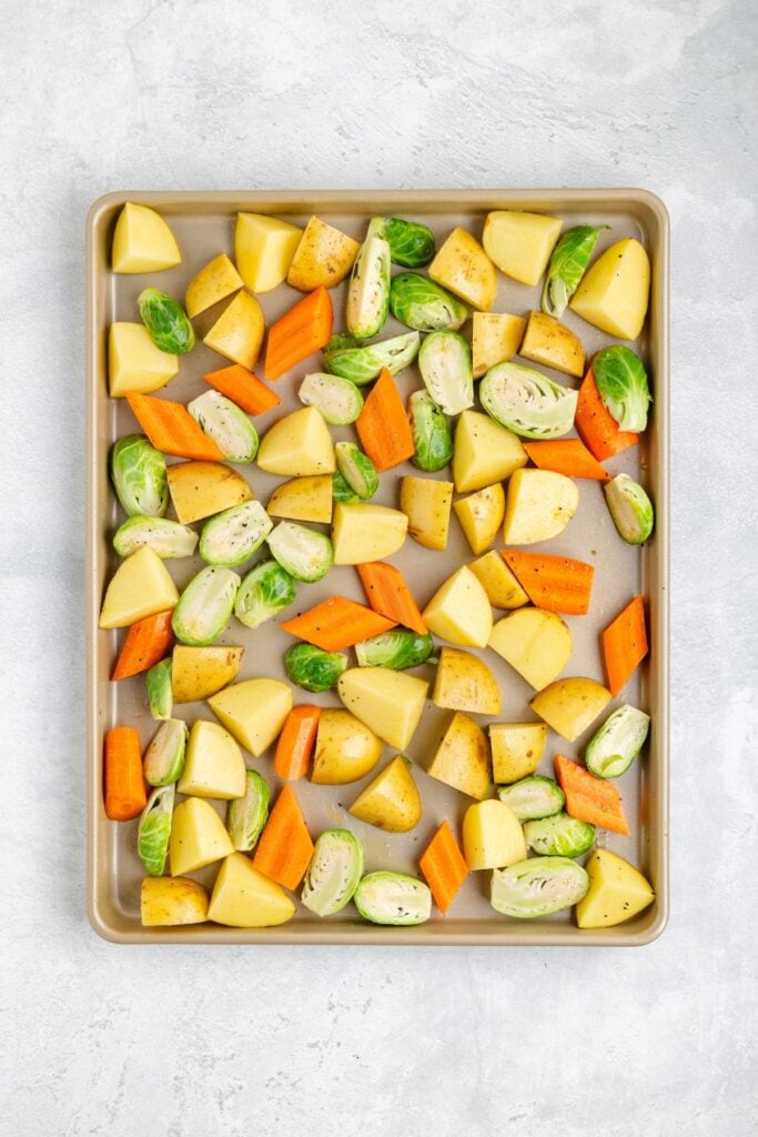 Chopped potatoes, carrots, and Brussels sprouts on a sheet pan, arranged for roasting in a single layer.