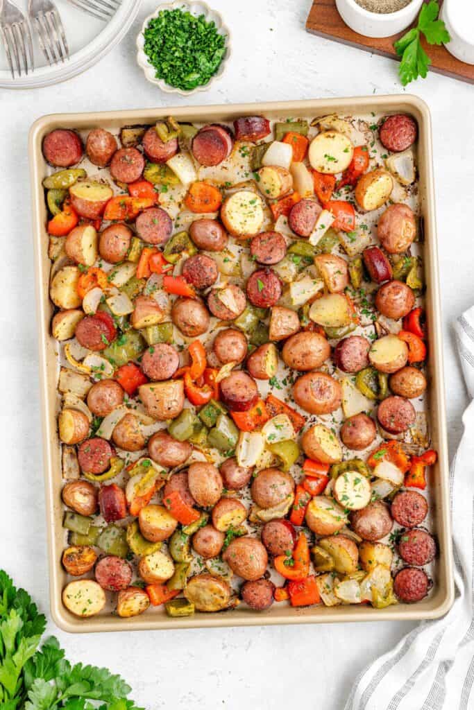 Sheet pan Sheet Pan Sausage, Potatoes, and Peppers with chopped herbs as garnish.