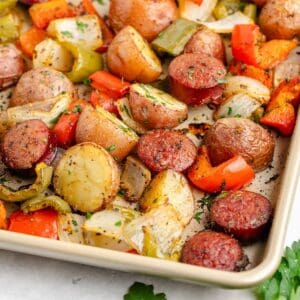 Sausage and potato sheet pan meal, with bell peppers, and onions, garnished with fresh herbs.