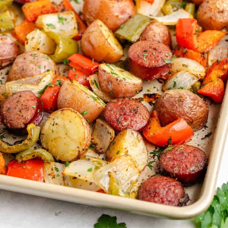 Sausage and potato sheet pan meal, with bell peppers, and onions, garnished with fresh herbs.