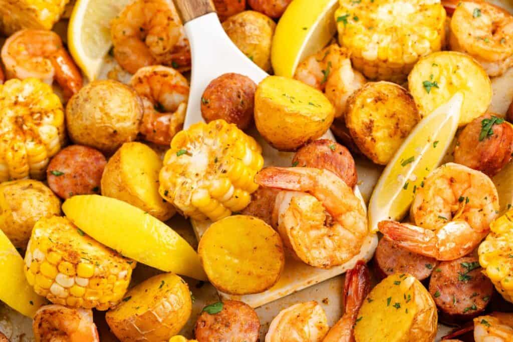 Close-up of a sheet pan seafood boil with shrimp, sausage, corn, potatoes, and lemon wedges.