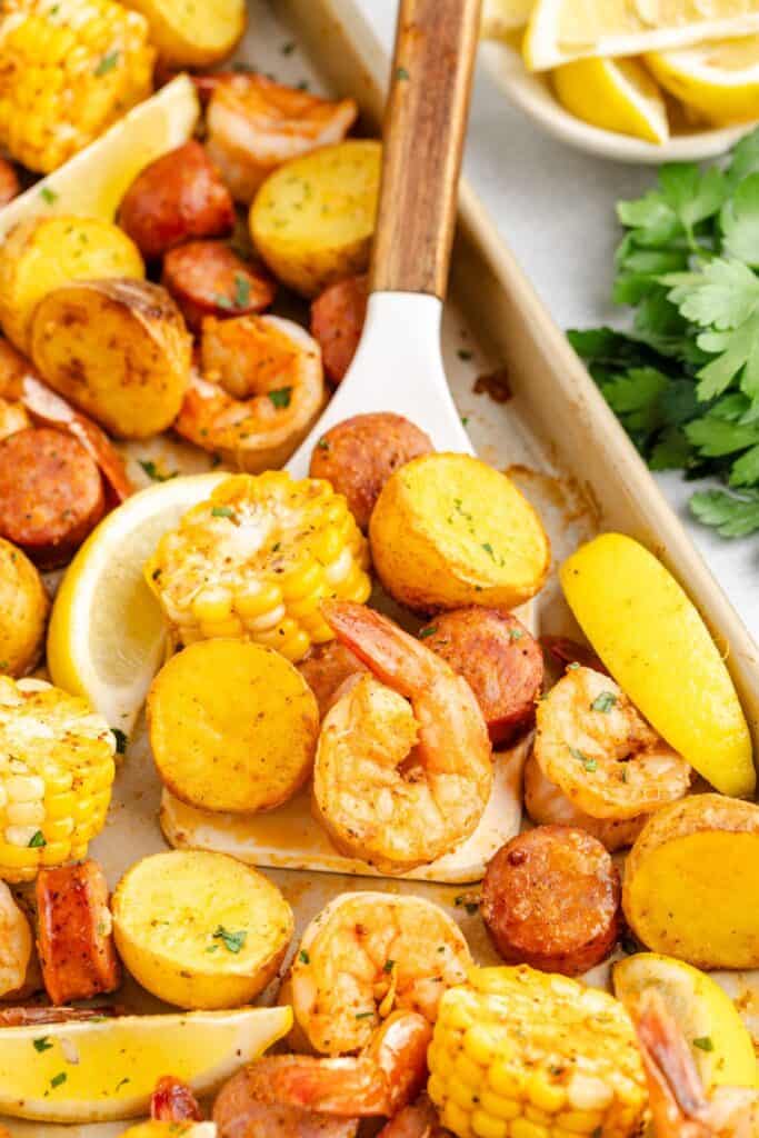 Sheet pan with cooked shrimp, sausage, corn on the cob, potatoes, garnished with lemon wedges and parsley.