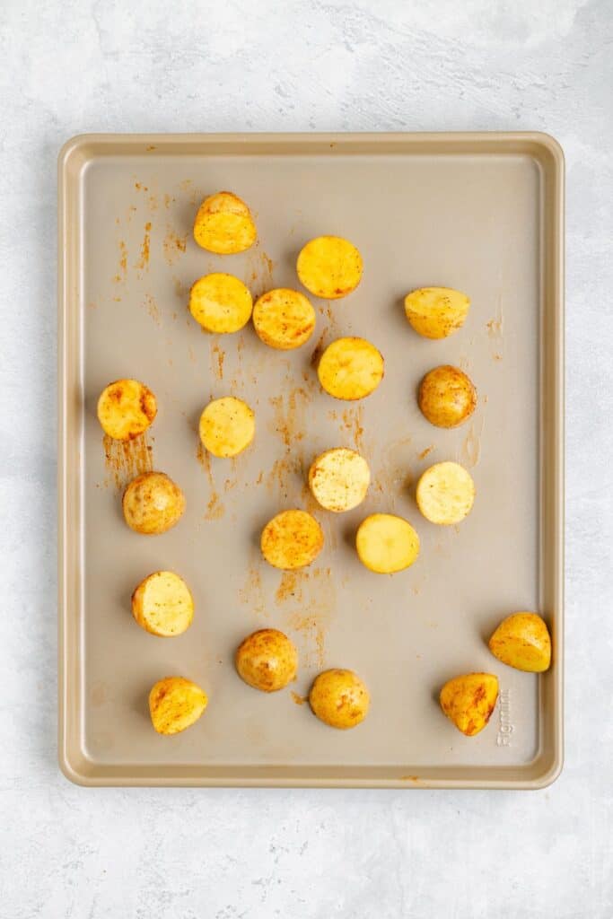 Halved, seasoned baby potatoes arranged on a baking sheet, prepared for roasting in the oven.