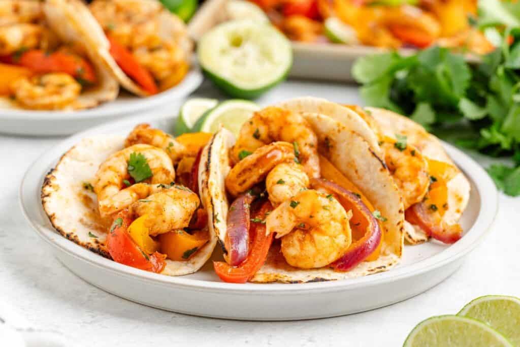 Shrimp fajita sheet pan with sautéed peppers and onions on flour tortillas, served with lime wedges and cilantro.