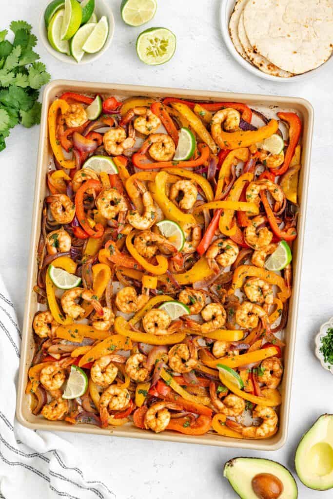 Baked Shrimp Fajitas with, bell peppers, onions, and spices; surrounded by tortillas, avocado, cilantro, and lime.