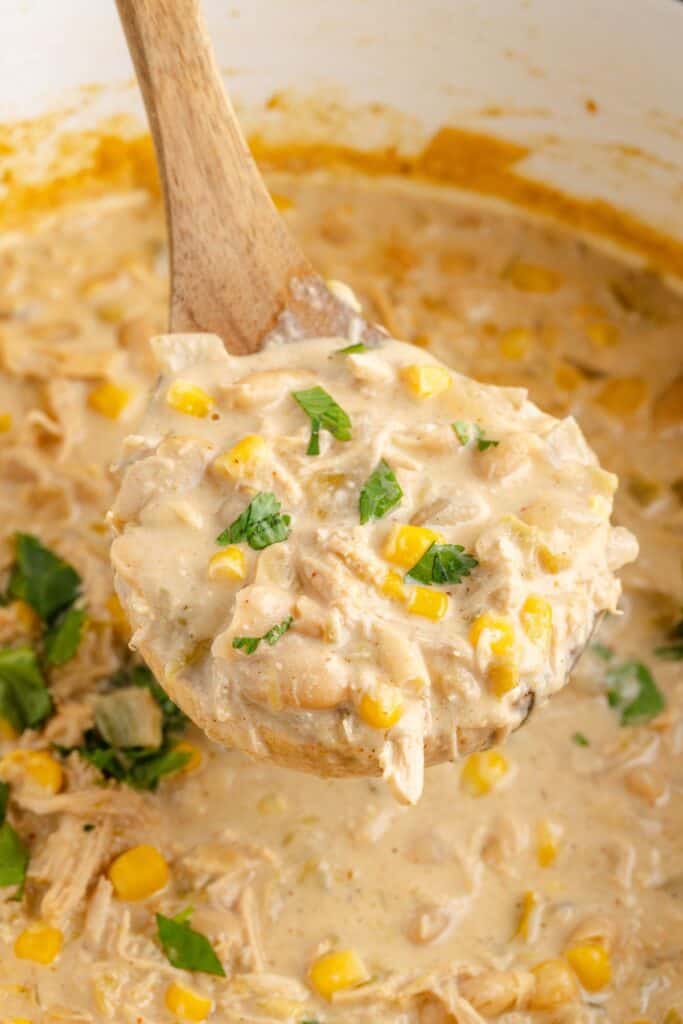 Wooden spoon lifting Creamy White Chicken Chili above a pot.