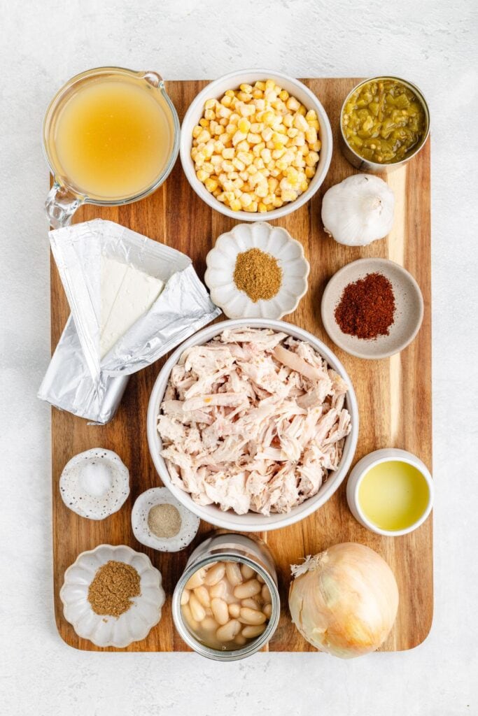 Various chili ingredients—shredded chicken, beans, corn, aromatics, spices—arranged in bowls on a wooden board.