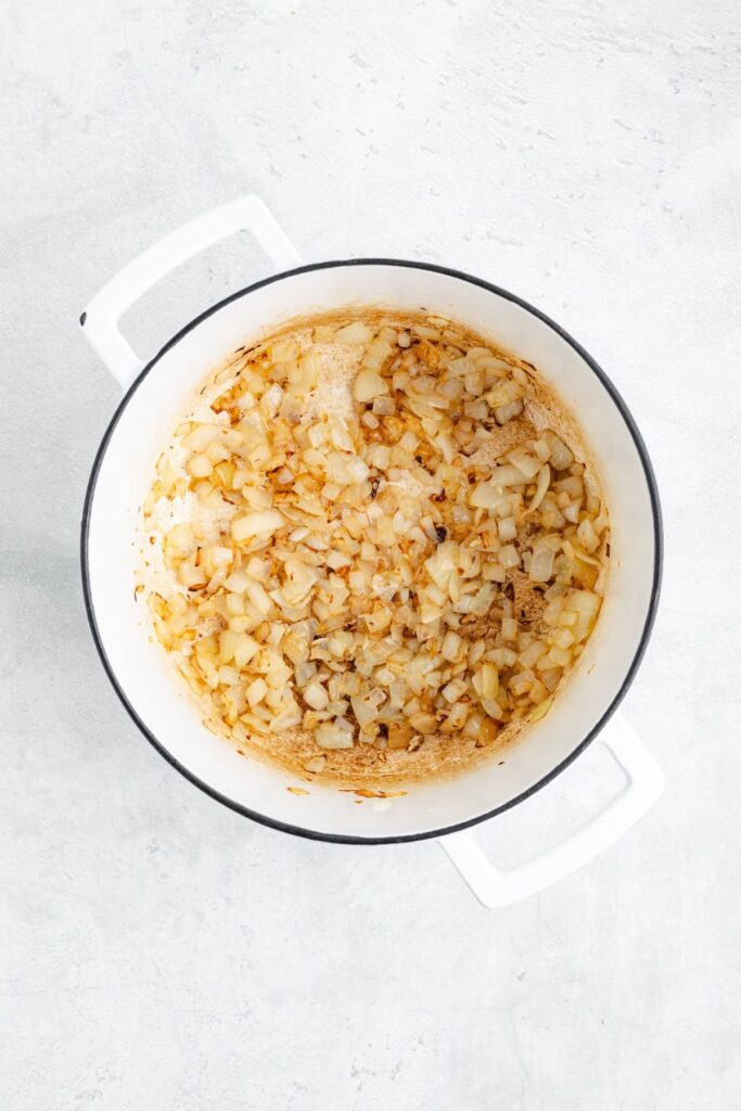 Chopped onions sautéing and browning in a white pot on a light gray countertop.