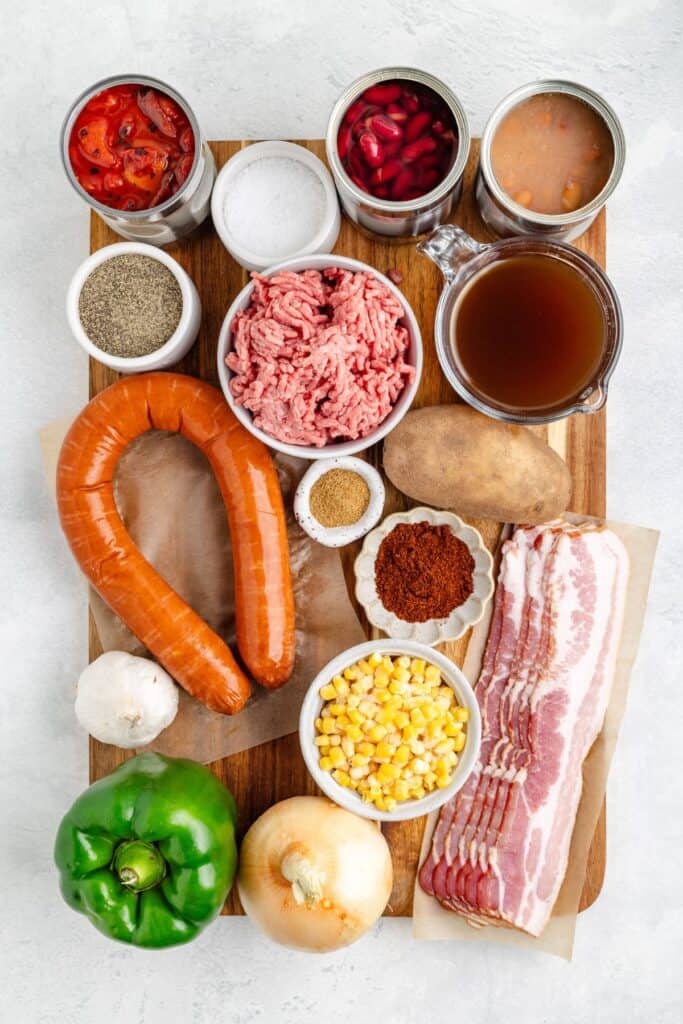 A wooden board topped with various ingredients, including meats, vegetables, beans, spices, and seasonings.