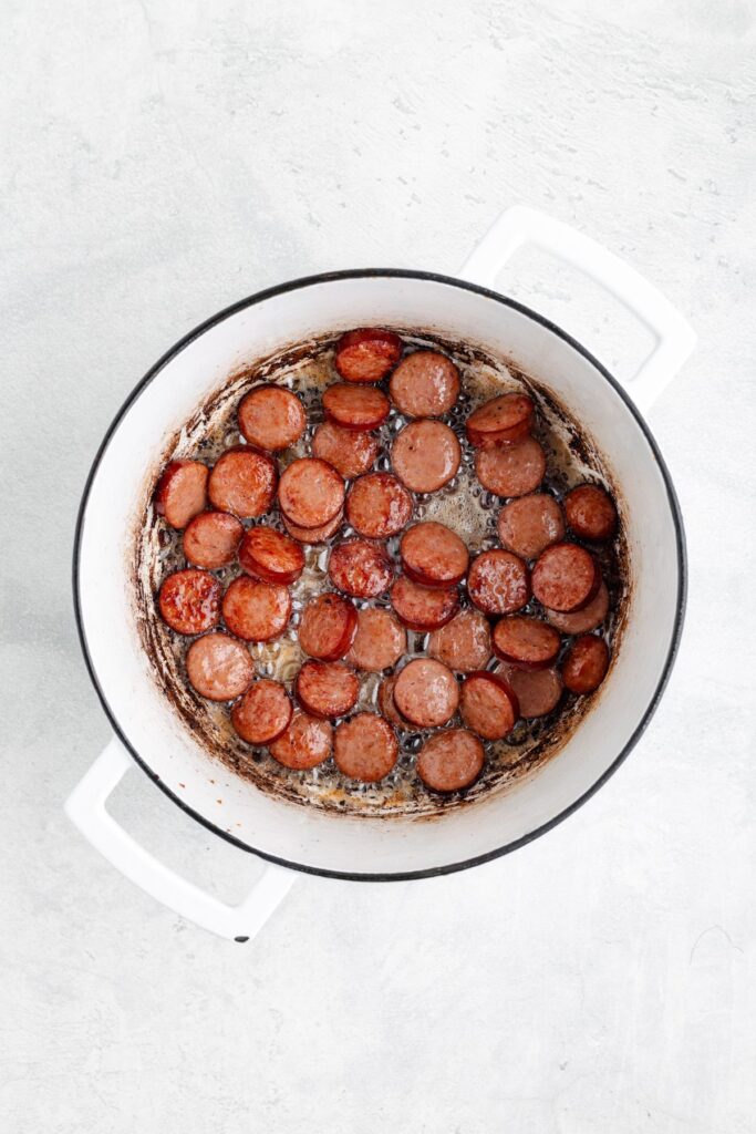 Browned sausage slices in a single layer inside a white pot, with sear marks on the bottom.