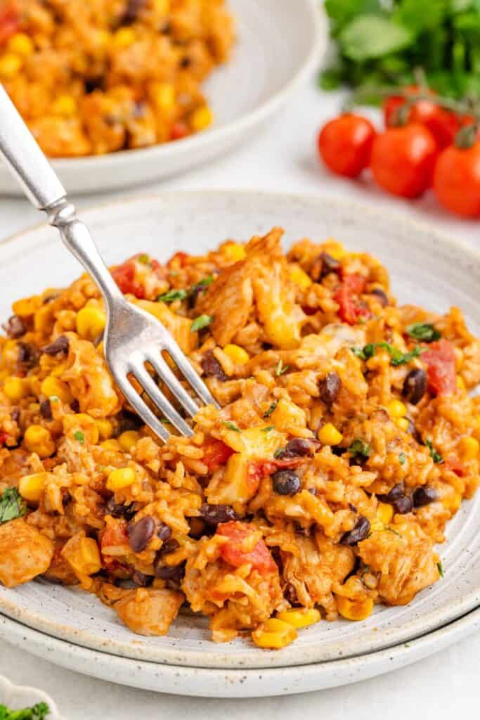 Cheesy Mexican chicken and rice with black beans, corn, and tomatoes on a plate with a fork.