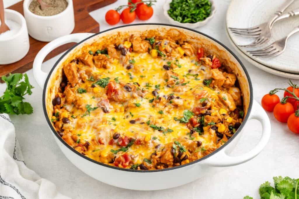Round casserole dish with Tex-Mex chicken and rice with beans, corn, tomatoes, and chicken, garnished with herbs.