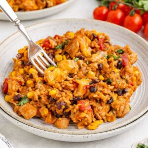Mexican rice with chicken, black beans, corn, and tomatoes, garnished with herbs and a fork on the plate.