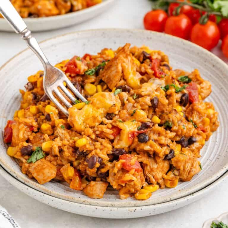 Mexican rice with chicken, black beans, corn, and tomatoes, garnished with herbs and a fork on the plate.