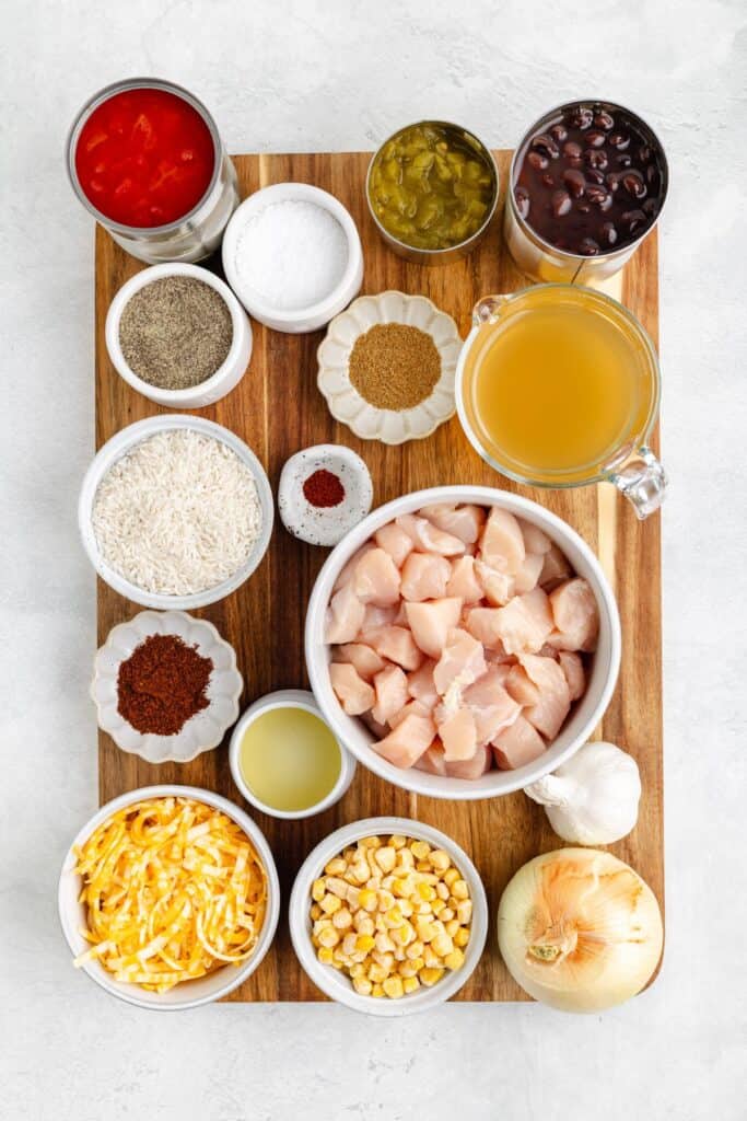 Bowls of chicken, rice, beans, corn, cheese, and other ingredients neatly arranged on a wooden board.