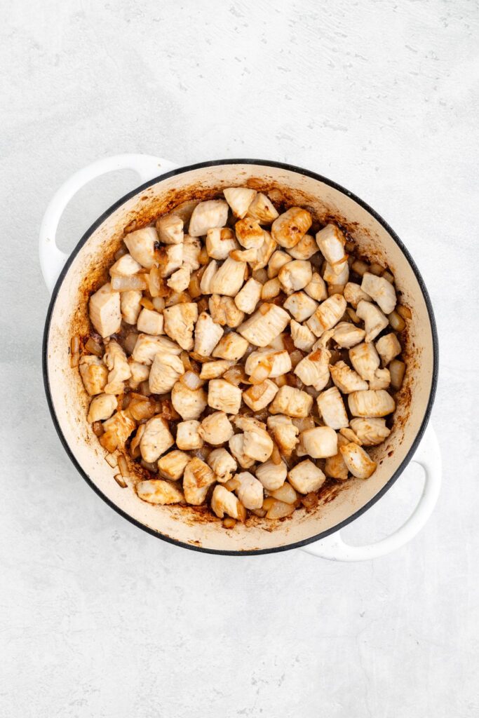 Cubed cooked chicken breast in a white pot with two handles on a light, textured background.