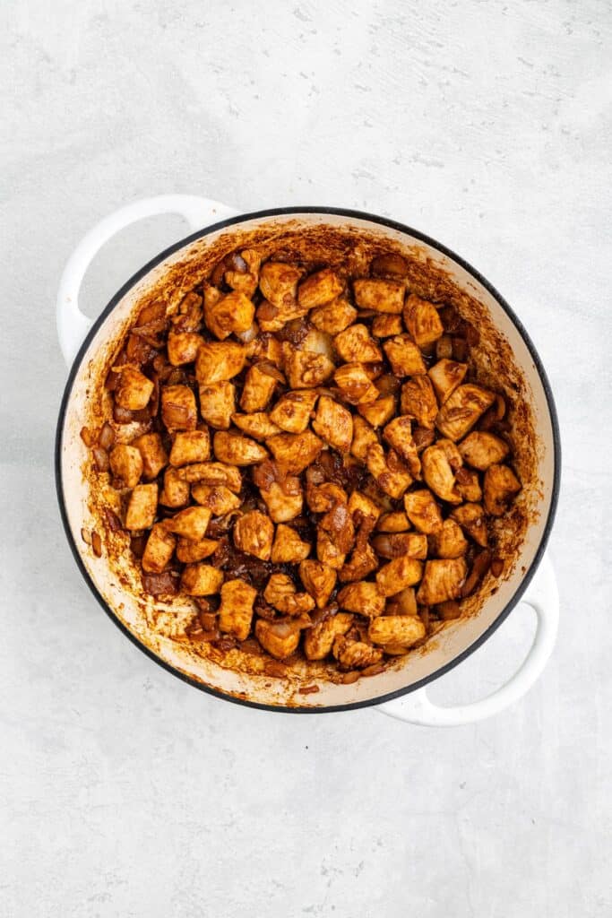 White pot with browned, seasoned chicken chunks on a light gray surface.