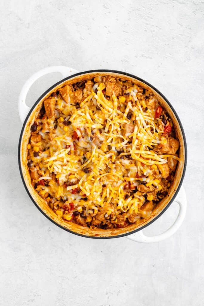A round white pot with cooked pasta, ground meat, corn, beans, tomatoes, and melted shredded cheese.