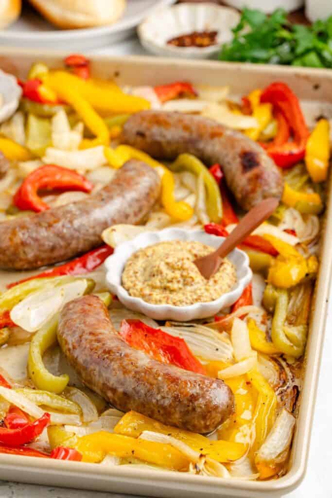 Sheet Pan Bratwurst and Peppers, and a small dish of mustard with a wooden spoon.