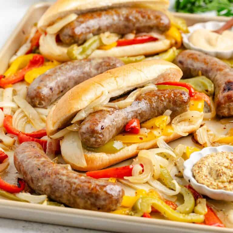 Bratwurst Sheet Pan Dinner with grilled onions and peppers on a tray, served with extra sausages and mustard.